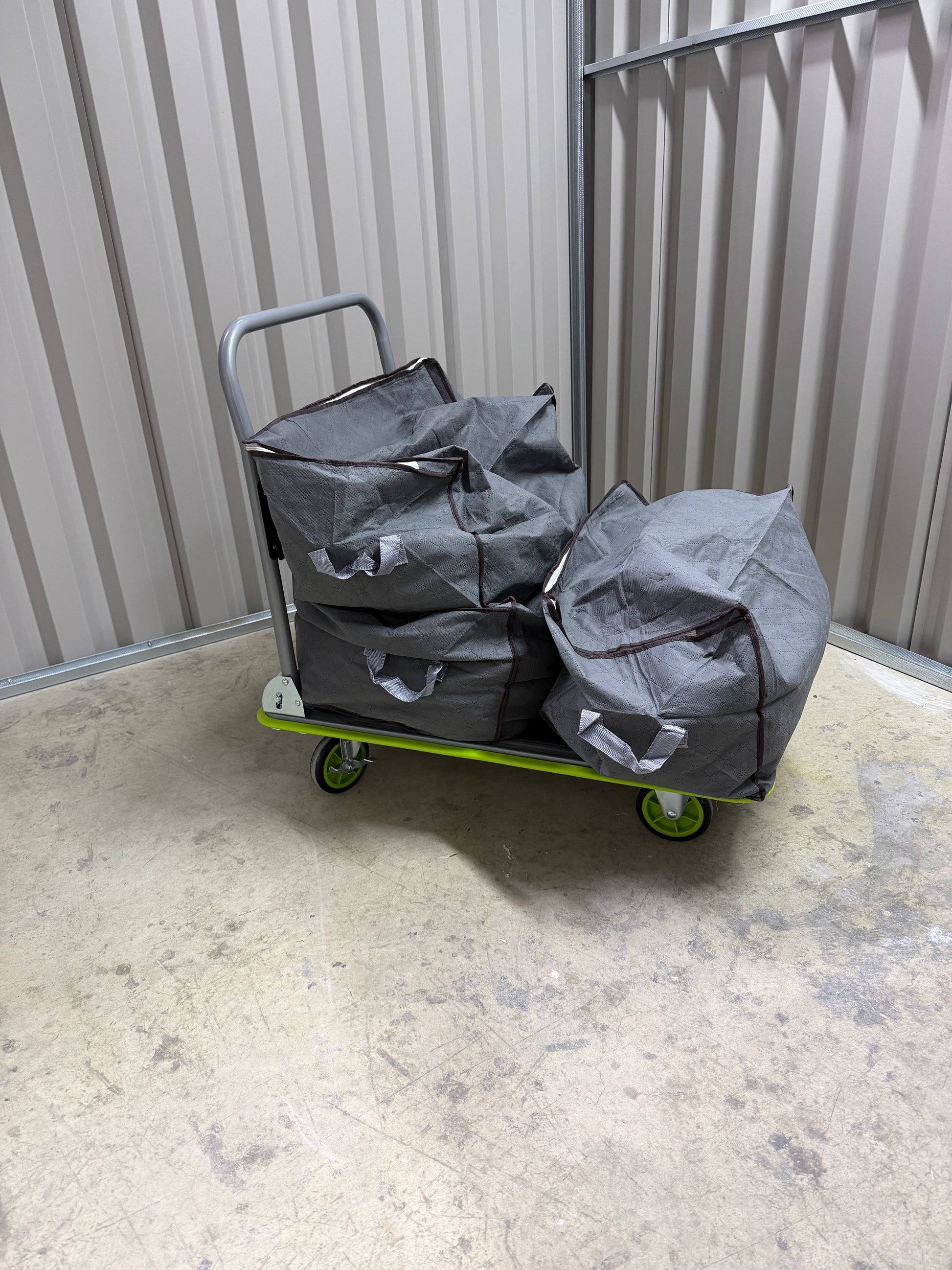 A customer's belongings (bags and boxes) on a complimentary trolley, placed inside a clean, secure, ground-floor Isle Store storage unit.