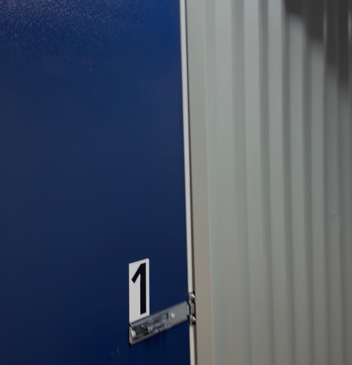 A close-up of a clean, blue metal door on an internal Isle Store storage unit, showing the secure silver latch mechanism ready for a padlock.