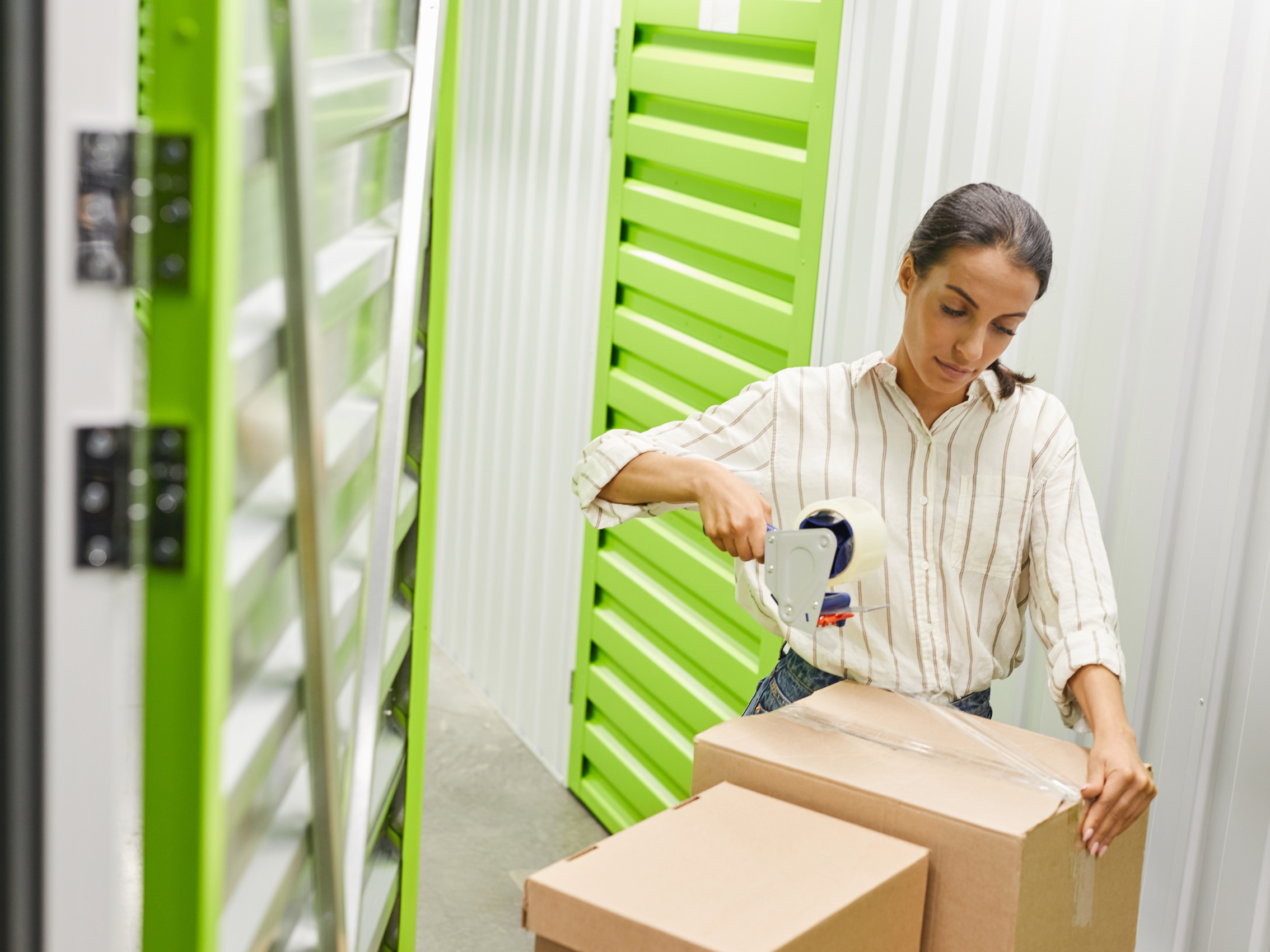 A customer preparing her belongings for storage by securely taping a cardboard box inside her clean, well-lit Isle Store storage unit.